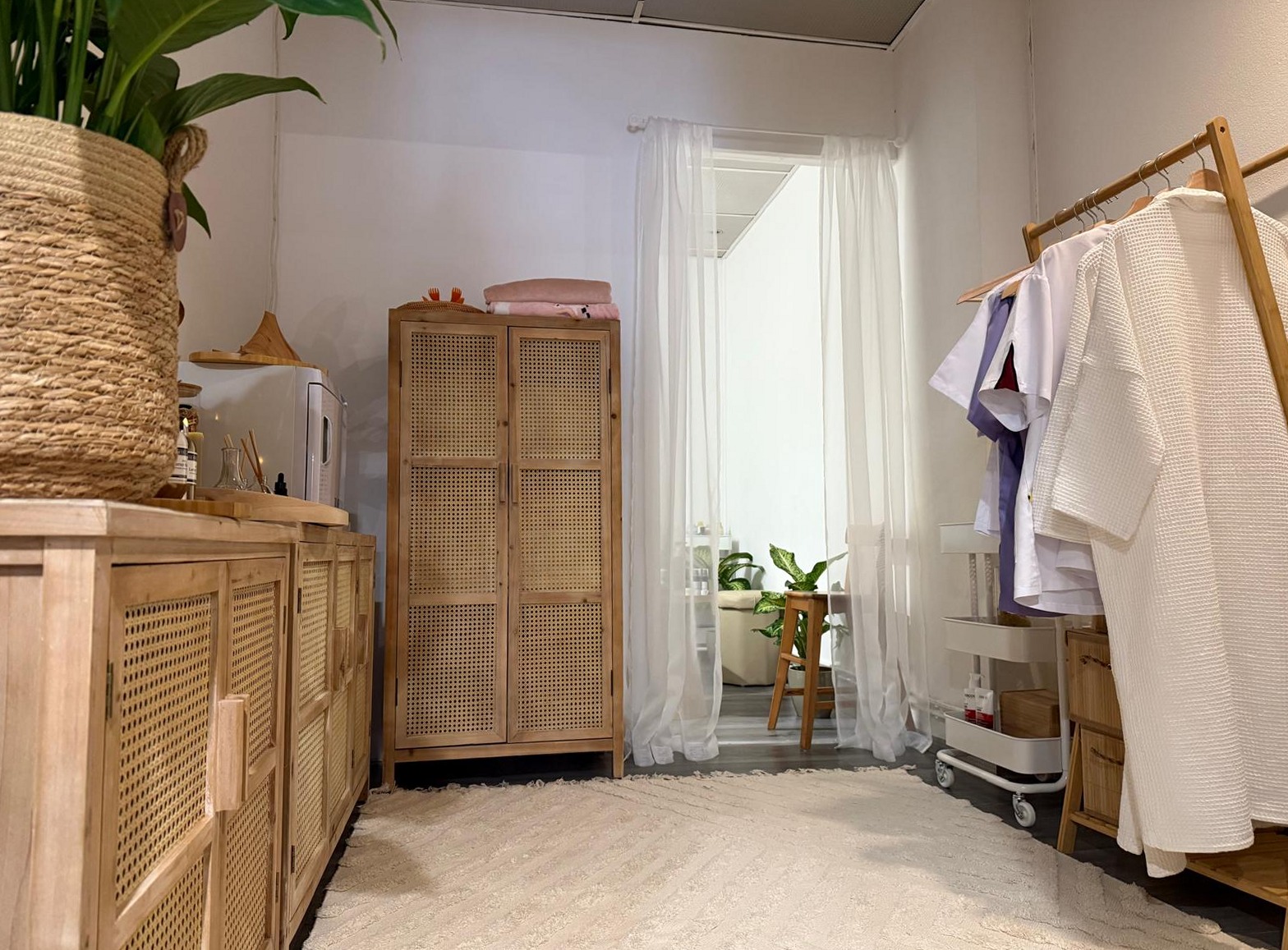 Behandelkamer met rotan kasten, planten en witte badjassen aan een rek