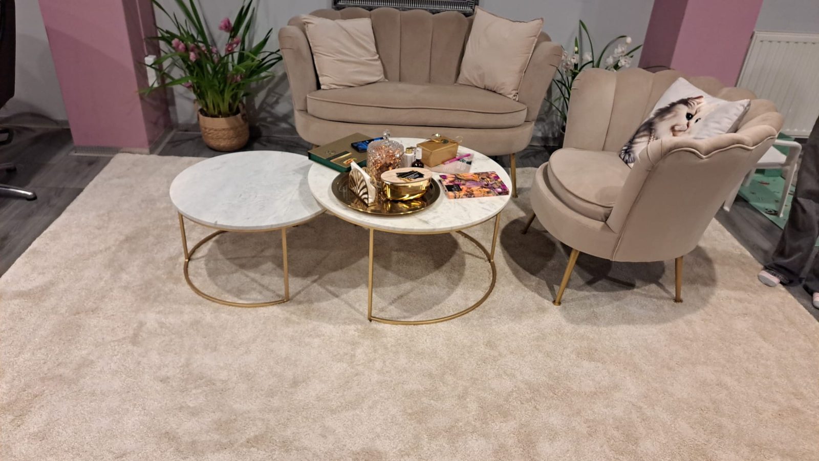 Wachtruimte met roze schelpstoelen, een bank en ronde marmeren tafels op een zacht vloerkleed