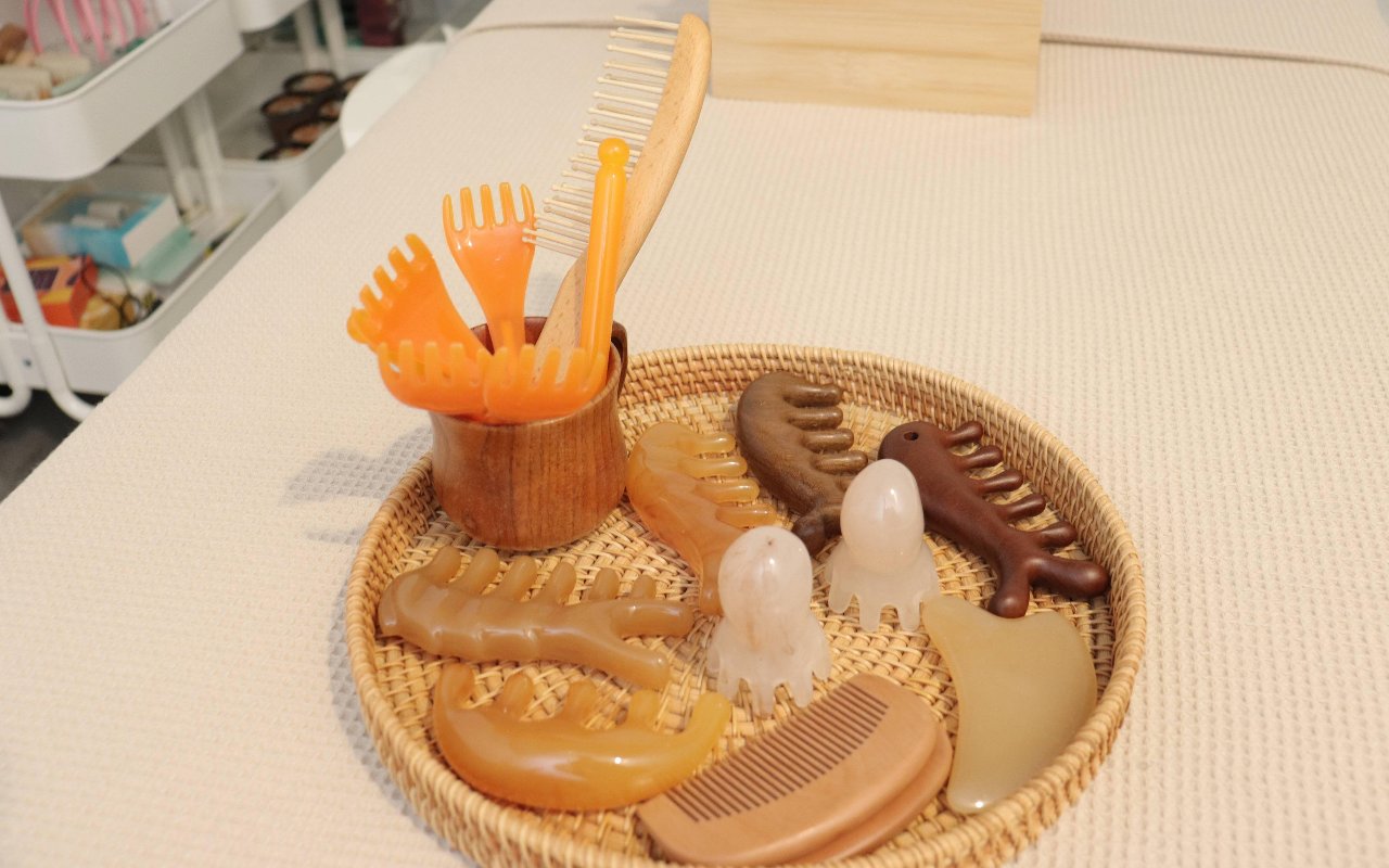 Houten kammen en gua sha-stenen in een rieten mandje op de behandelbank
